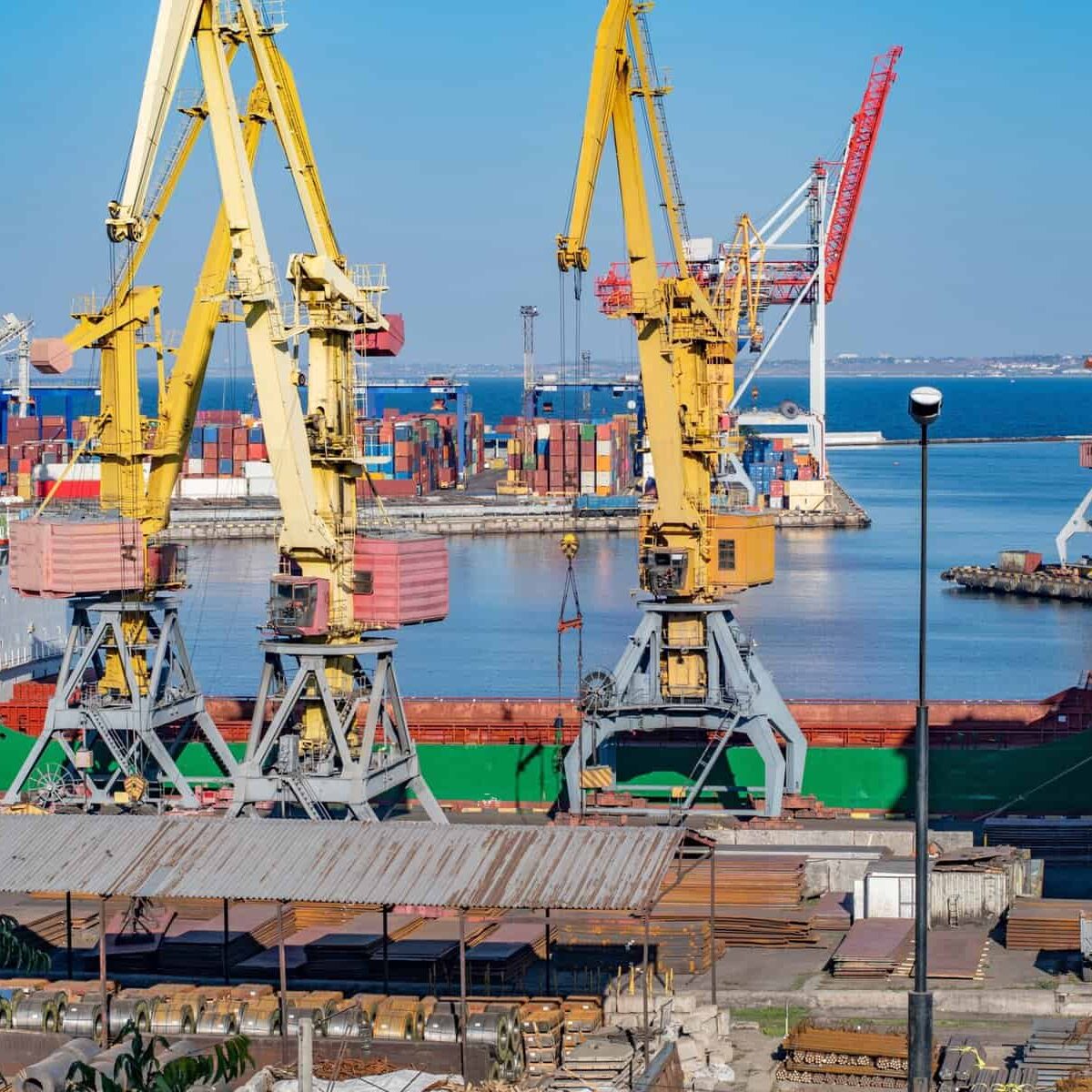 Industrial seaport with heavy loading machinery and metal cargo goods and containers. Port harbor with yellow shore cranes